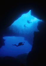Diver underwater photographer swims dives through large underwater cave grotto Blue Dome Blue Hole on west coast of Gozo Island