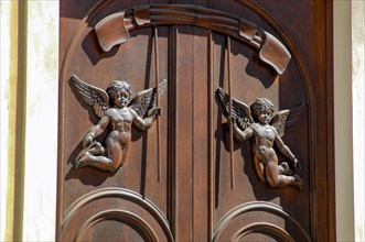 Old wooden front door with attached wood carving in the shape of floating angels two angels with wings
