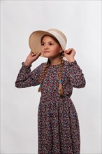 Portrait of a girl holding her sun hat tightly against a white background