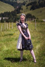 Blonde woman in black designer dirndl made of laceand bag on a mountain meadow