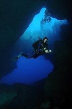 Diver with underwater lamp swims dives through large underwater cave grotto Blue Dome Blue Hole on west coast of Gozo Island