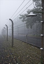 Reconstructed camp fence with crematorium in the fog at beech forest concentration camp