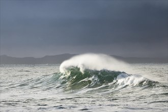 Big wave breaks in winter storm in open sea and dramatic light off north coast of Ireland