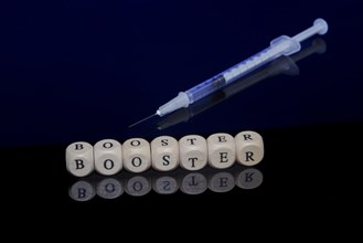 Medical vaccination syringe with the word booster formed from letter cubes on a dark background