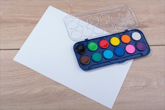 Watercolor paint box on a sheet of paper a wooden background