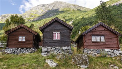 Three wooden huts stand on a mountain in Norway