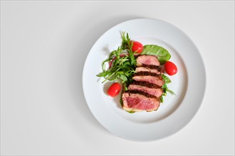 Top view of grilled duck breast medium rare served on a plate with arugula and corn salad