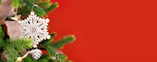 Christmas banner with tree branch with natural wooden snowflake ornament in front of red background with copy space