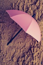 Pink umbrella on sand seen from the top