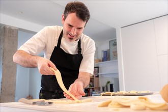 A man baking croissants picking up the triangular cuts from the puff pastry
