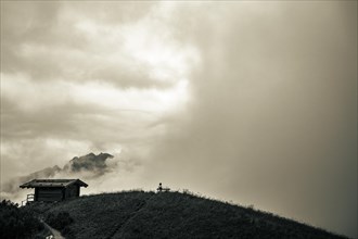 Mountain hut with bench and climber and dramatic clouds in the background
