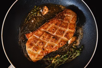 Top view of crispy crosswise cut duck breast in frying pan with thyme and garlic