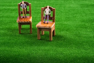 Men figures on wooden toy chairs on artificial grass