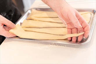 Detail of the hands of a man baking croissants making triangular cuts in the puff pastry and placing them on a tray