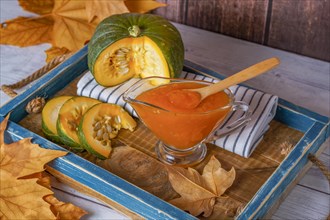 Homemade pumpkin marmalade in a glass jar on a wooden tray with dried leaves