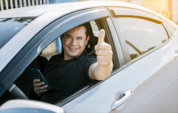 Smiling driver holding cellphone showing thumb up. Driver man showing thumb up while holding cellphone. Happy driver giving a thumbs up on the road. safe driving concept