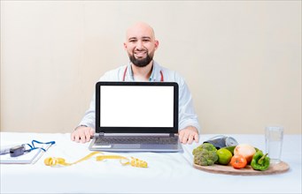 Nutritionist man showing laptop screen. Nutritionist at desk showing blank screen of laptop. Smiling nutritionist showing an advertisement on the laptop