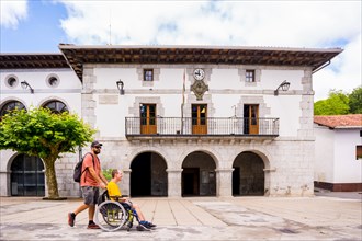 A disabled person in a wheelchair walking through the town square having fun with a friend