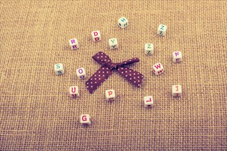 A ribbon and scattered dice-sized alphabet cubes on a textured surface in display