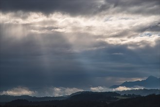 Rays of sunshine fall through impressive cloudy skies onto the mountain landscape around Murnau