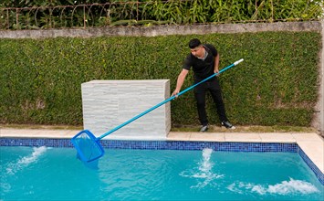 Swimming pool cleaning and maintenance concept. Maintenance person cleaning a swimming pool with skimmer
