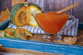 Homemade pumpkin marmalade in a glass jar on a wooden tray with dried leaves