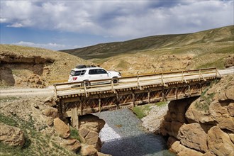 Four-wheel drive car crossing a wooden bridge over a wild gorge
