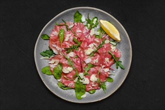 Top view of marbled beef carpaccio with arugula and chard leaves