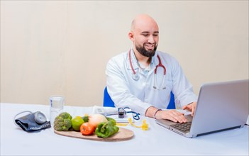 Nutritionist doctor using laptop at workplace. Bearded nutritionist doctor working on laptop at desk