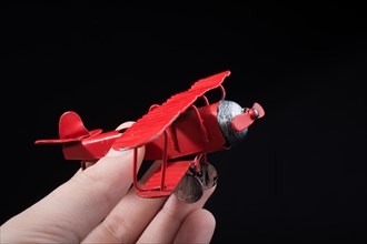 Hand holding a red toy plane on a black background