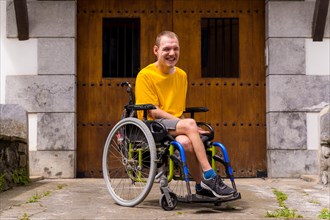 Portrait of a disabled person dressed in yellow in a wheelchair in the entrance of his house smiling
