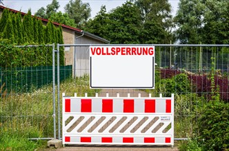 A closed path with a barrier and a construction fence with a rectangular board with a lot of text space with the word FULL CLOSURE