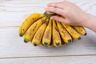 Hand holding bunch of freckled bananas on a wooden texture