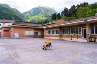 A disabled person dressed in yellow in a wheelchair in the schoolyard