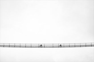 Suspension bridge with two cyclists against a white sky
