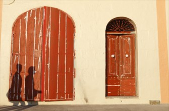 People casting shadows on red doors