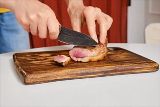 Hands holding fried duck breast and cutting it on slices