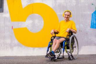 Portrait of a disabled person dressed in yellow in a wheelchair smiling listening to music
