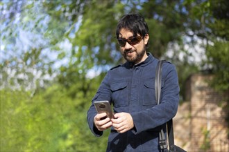 Happy young handsome Hispanic hipster man using phone at the park