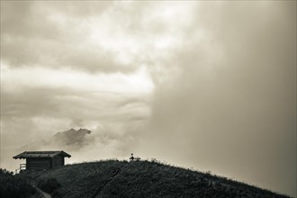 Mountain hut with bench and climber and dramatic clouds in the background