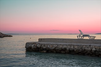 Lonely sun lounger standing on a jetty with reddish evening sky in the background