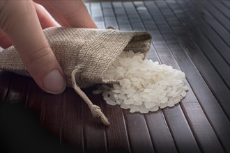Hand holding straw pouch full of uncooked rice on a wooden background