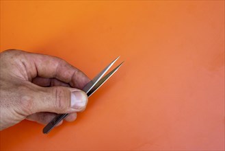 Male hand holding a pair of medical tweezers against an orange background