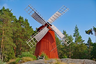 Small red wooden windmill at the edge of the forest
