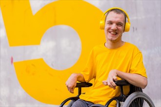 Disabled person dressed in yellow in a wheelchair smiling listening to music