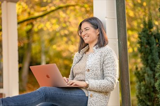 Pretty woman with glasses and MacBook in hand sits in the park at autumn time