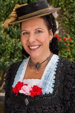 Beautiful young woman in Bavarian traditional costume wears a traditional dirndl with hat Her hair is neatly braided and she has three red and pink flowers in her bodice