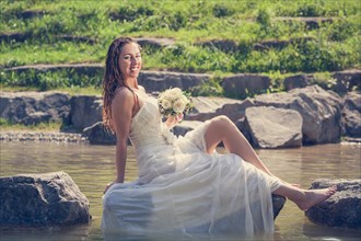 Bride in wet dress sits on a stone