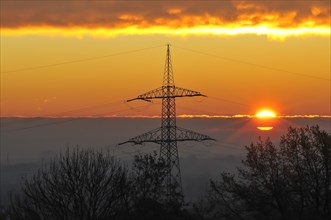 Backlight shot of a sunrise in front of an overhead power line mast in Bavaria