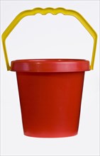 A bright red plastic childs bucket with a yellow handle